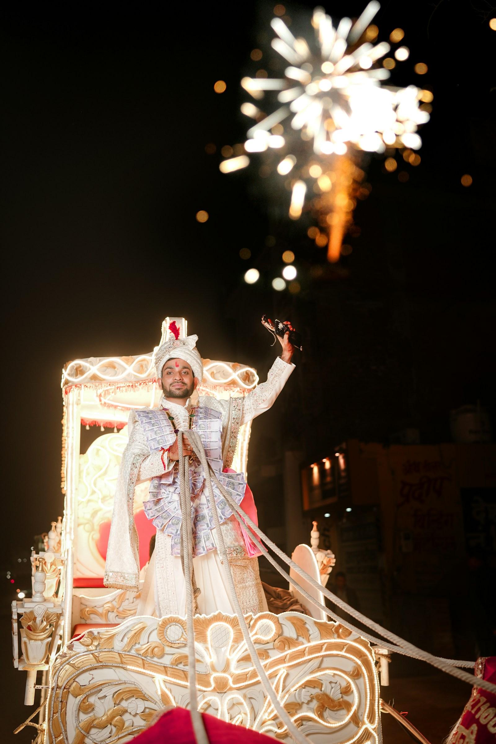 A groom arriving by lit carriage, fireworks over the baraat