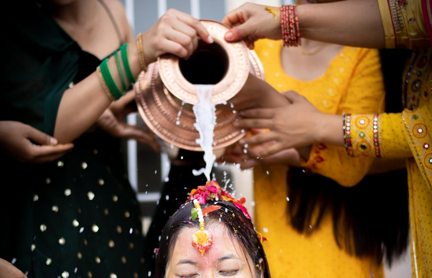 Groom in a yellow kurta on a marigold-and-gold mandap with bright turmeric powder thrown in the air around him during his haldi ceremony